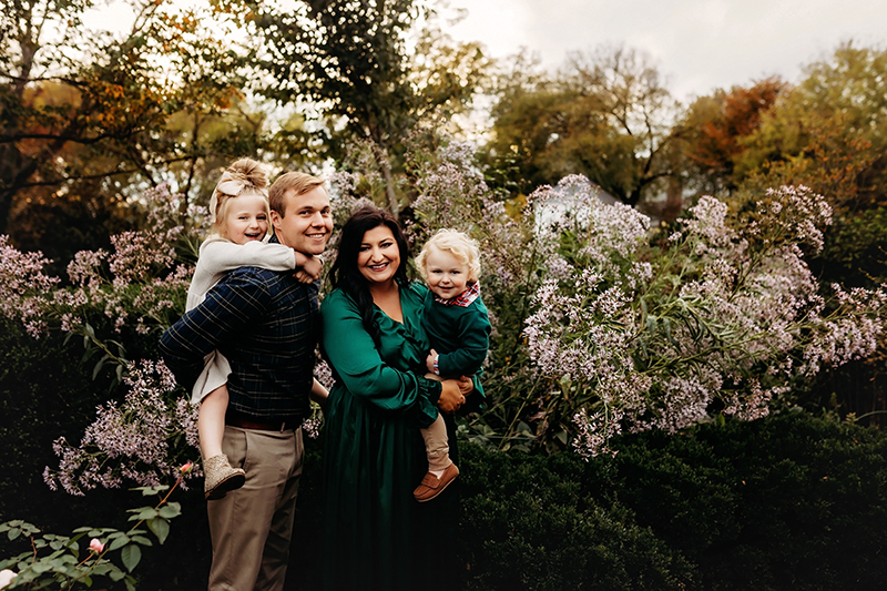 midlothian photographer, mom and dad each holding kids in front of flowering bush at Tuckahoe Plantation