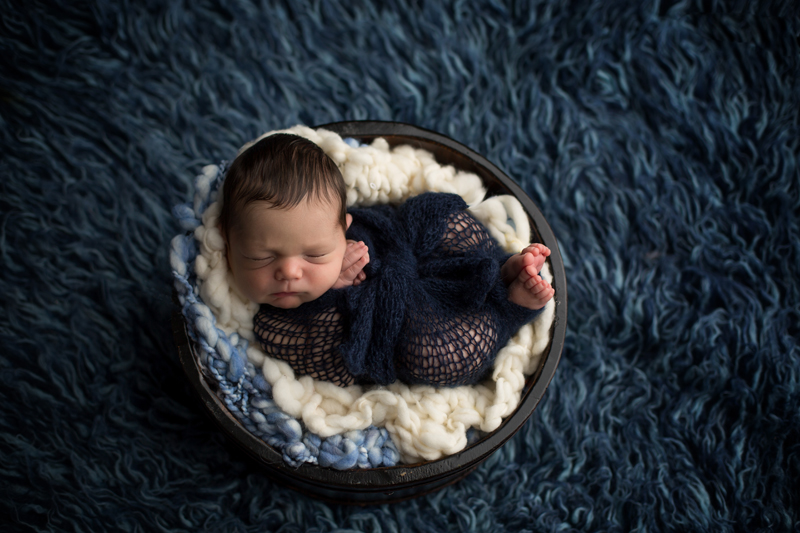 Moseley, Virginia newborn photographers, newborn boy asleep in navy knit wrap in brown bowl on navy blue rug