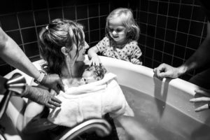 Richmond birth photographer mom in tub with just born newborn looking at big sister
