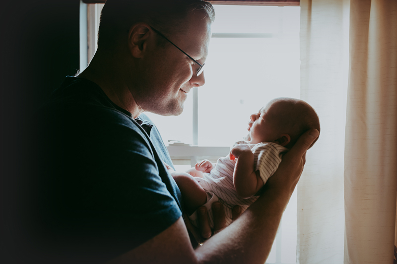 newborn lifestyle session rva, dad holding newborn boy in front of window and looking at him smiling