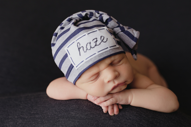 Midlothian, Virginia newborn photographers, newborn baby boy with his chin on his hands while he's asleep on a gray backdrop and a striped sleepy cap