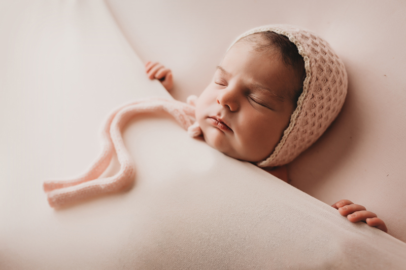 Richmond photographers, newborn baby girl asleep on her back with pink backdrop and pink knit bonnet