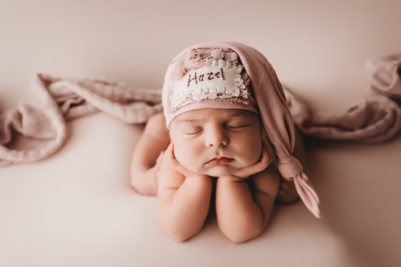 Richmond, Virginia photographer, newborn baby girl with club feet on pink backdrop in froggy pose with pink sleepy cap and the name Hazel sewn on it
