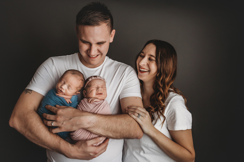 Midlothian, Virginia newborn photographer, dad holds newborn twins in his arms while mom looks on and laughs