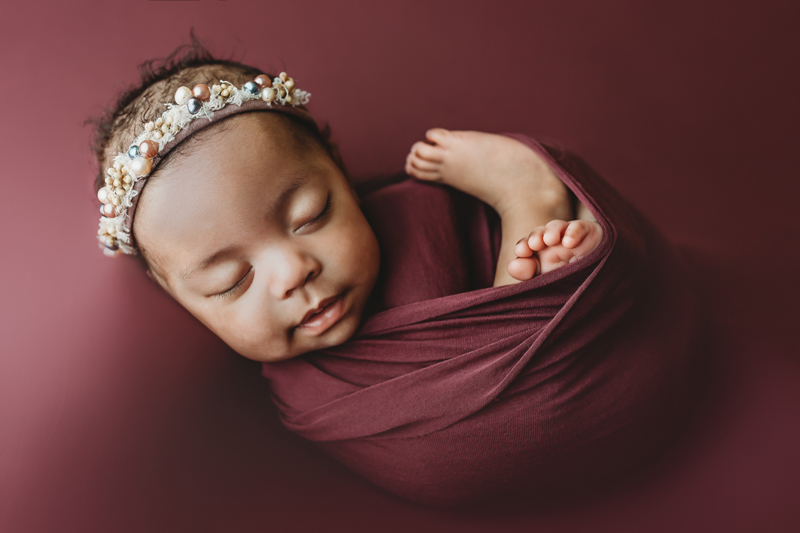 Oklahoma City, Oklahoma newborn photographer, black newborn baby girl wrapped in dark mauve fabric with headband with pearls on fabric background