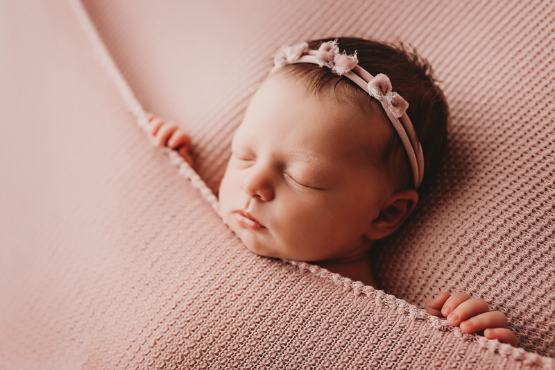Oklahoma City, Oklahoma newborn photographer, sleeping newborn baby girl on pink background with tiny pink headband with bows