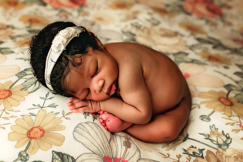 Chester, Virginia newborn photographer, black newborn girl asleep on flowery backdrop with her feet and hand folded underneath her head