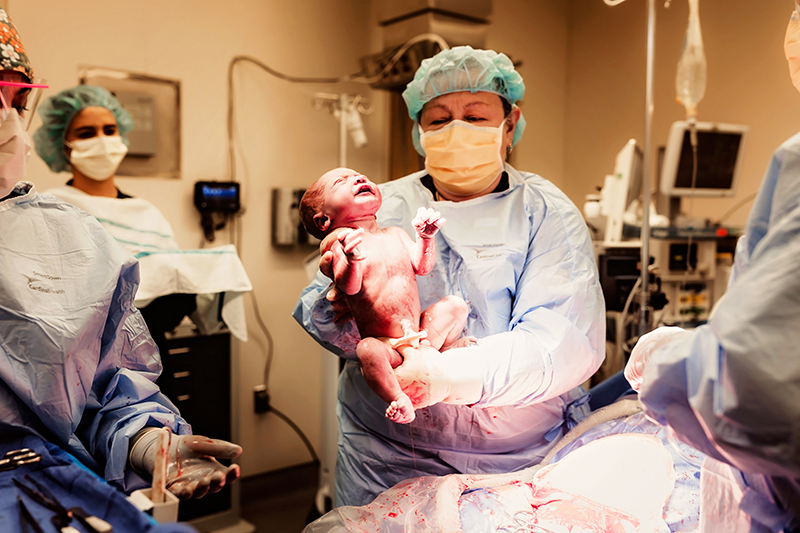 Richmond, Virginia birth photographer, OB holding newborn in OR up to the camera over the OR table