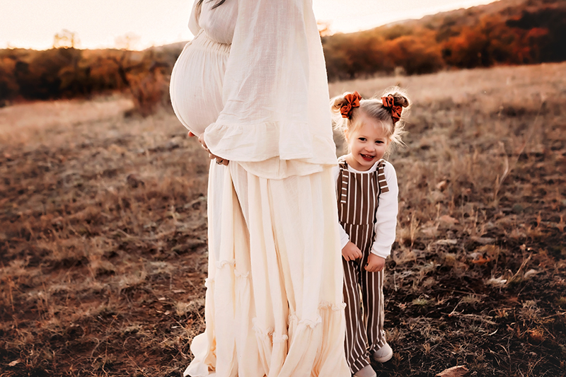 Wichita Falls photographer, woman with hands on pregnant belly with daughter peeking from behind her