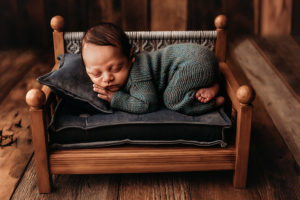Richmond photographer, newborn boy in blue knit outfit lying on his stomach on a wood bed