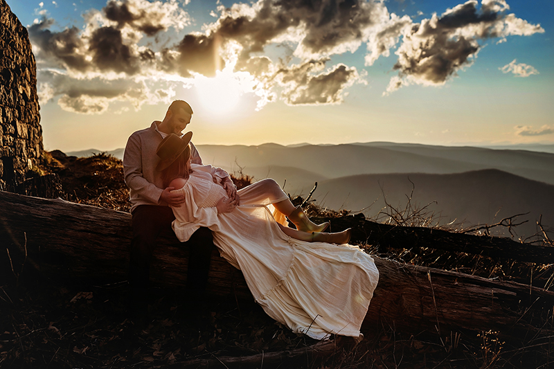 Pregnant mama lying on her husband's lap wearing a white dress and brown hat looking over mountains of Charlottesville photographer, Richmond maternity photographer, rva photographer, 