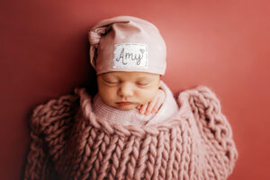 Newborn baby girl in dusty pink sleeping with name on her hat which says Amy, Midlothian newborn photographer