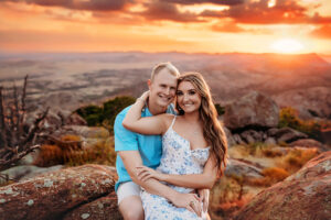 White couple embracing and looking at camera on top of Mount Scott with vivid orange backdrop