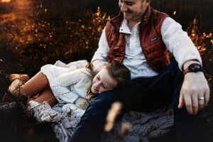Blonde hair daughter lying on the ground with her head on her dad's lap. 