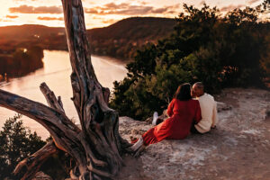 Richmond Couple sitting on edge of cliff overlooking sunset and river kissing