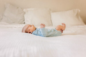 Richmond newborn photographer with baby lying on his back in blue onesie on white comforter.