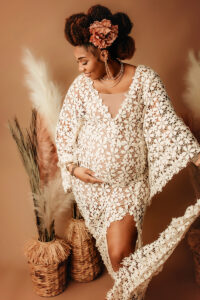 Black mama with ivory flower dress with pampas grass on light mocha colored backdrop holding her pregnant belly in Richmond, VA.