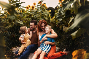 Richmond family photographer family sitting on ground in sunflower field laughing and smiling